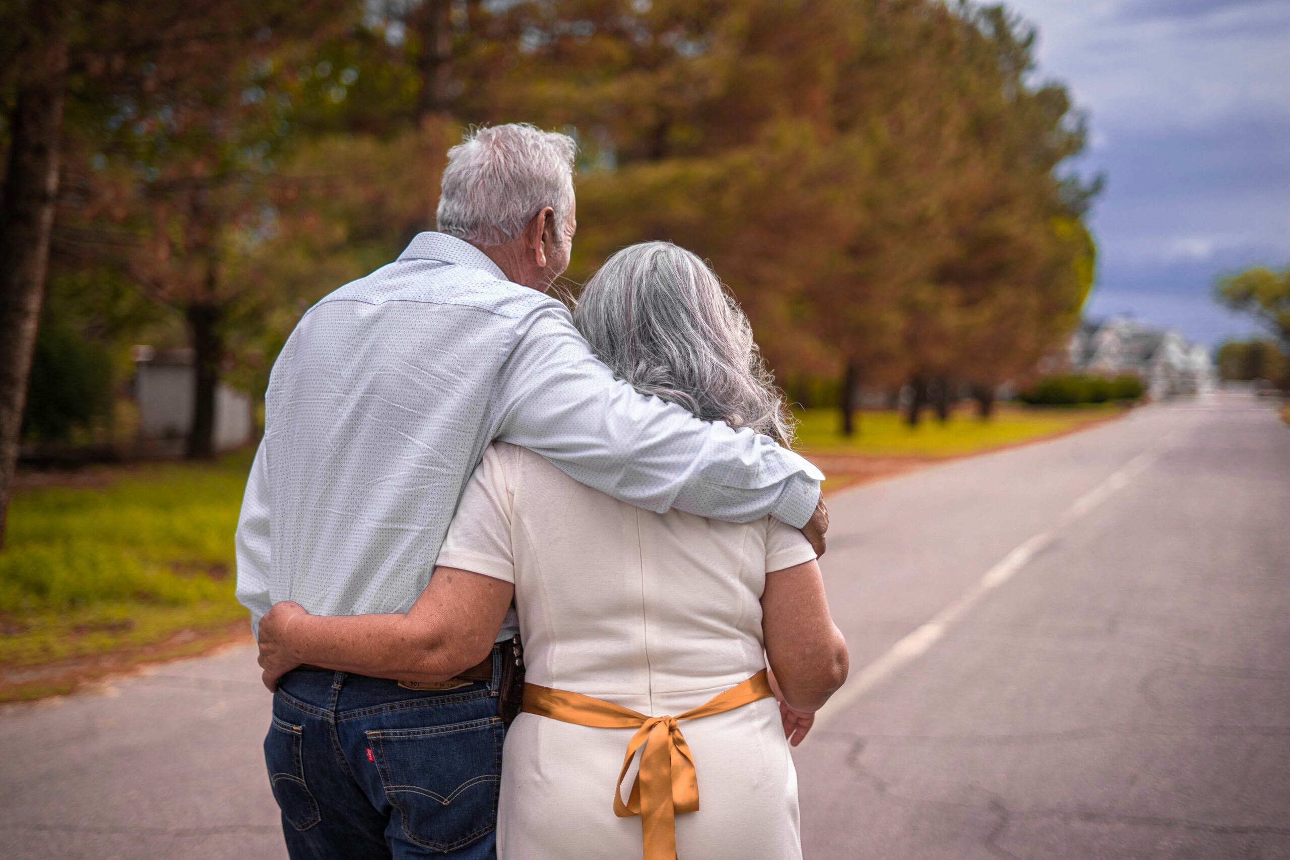 Elderly couple walking down the road with their arms around each other.